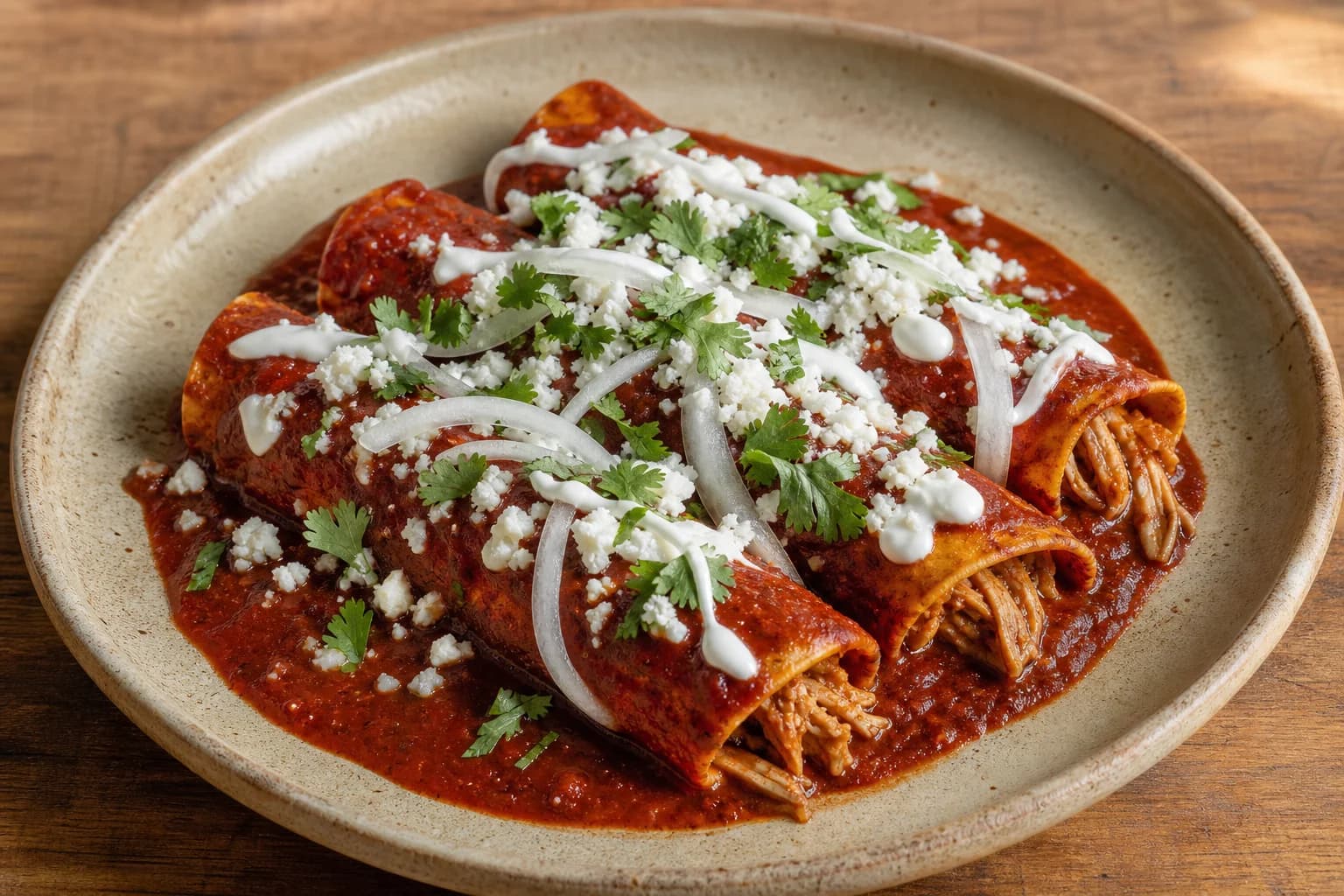 Red chicken enchiladas with soft corn tortillas, guajillo-ancho sauce, queso fresco, crema, onion, and cilantro.
