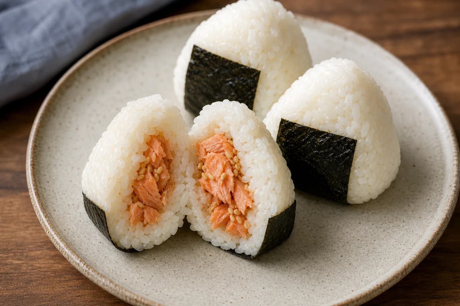 Japanese salmon onigiri shaped into neat triangles with plain short-grain rice, salted roasted salmon filling, sesame, and crisp nori strips.